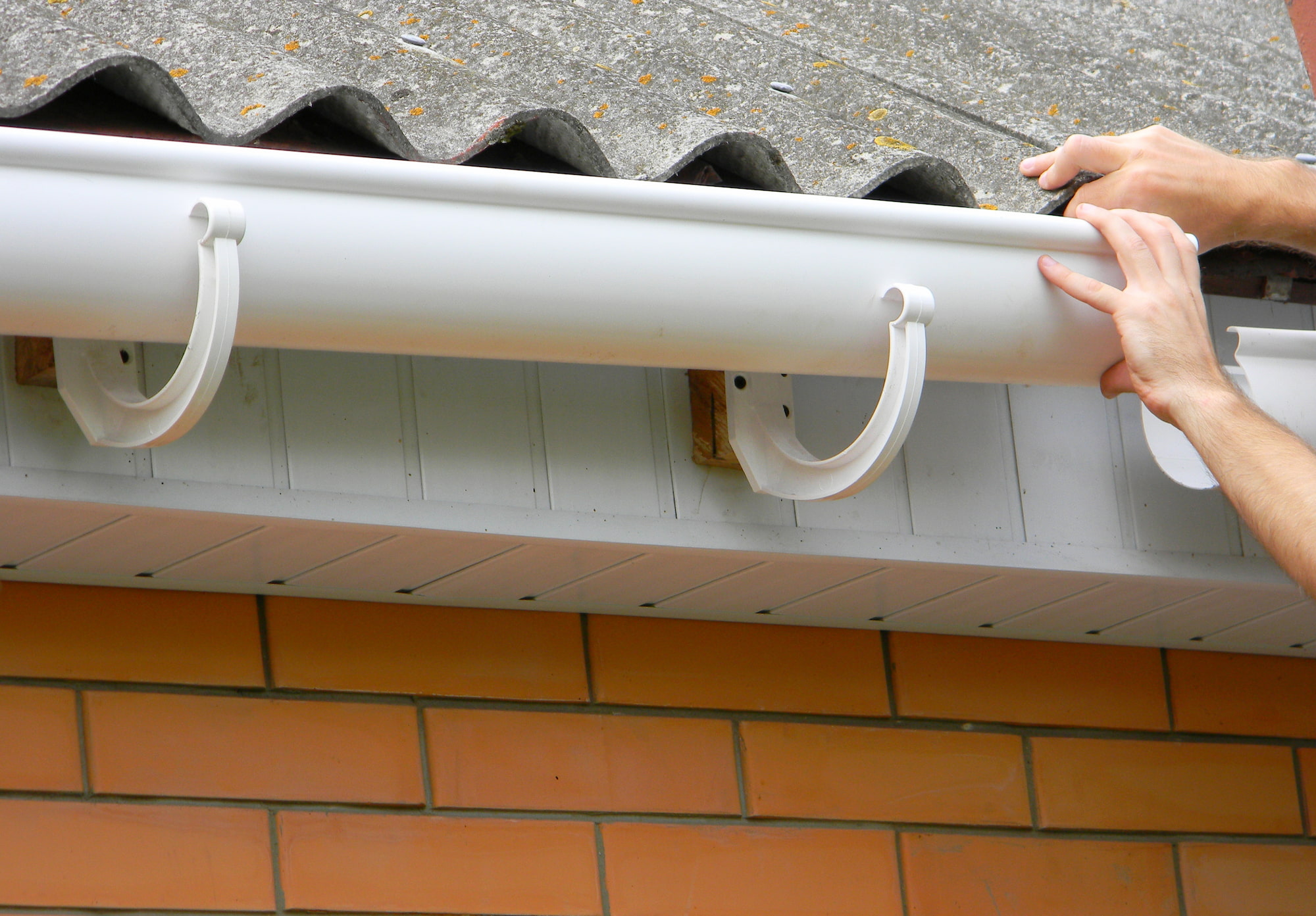 White gutter being installed on a brick house.